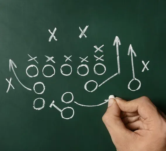 A green chalkboard where a hand is drawing an offensive and defensive game plan