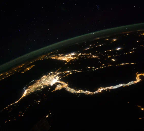 A satellite view of Earth at night, showing cities glowing with their lights