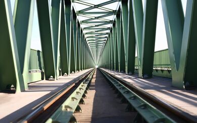 A tunnel view of a green train track with a towering green bridge frame on the sides and above
