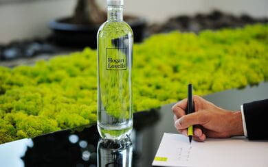 Hogan Lovells branded water bottle in a conference room with a person taking notes