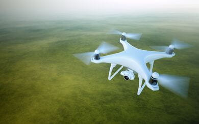 A white drone flying above a green area