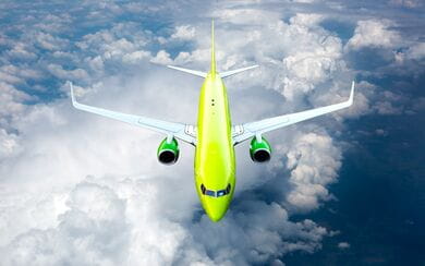 Top front view of a lime green passenger plane flying in the sky above the clouds