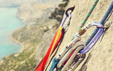 Rock climbing carabiners and ropes hang from a cliff overlooking a mountainous beach