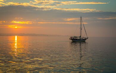  A small boat on the ocean, standing out against the orange horizon, representing the Insurance Horizons report from Hogan Lovells