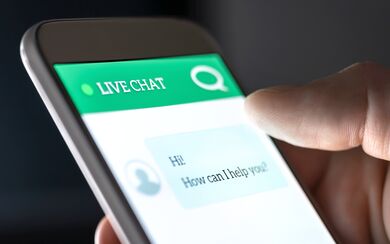A hand holding a smartphone displaying a live customer service chat with a chatbot and automated messages
