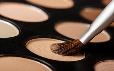 A close-up of a neutral powder makeup palette with a small brush dipped in a single color