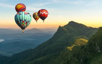 Aerial view colorful hot air balloons flying over a mountain range with an orange horizon in the background