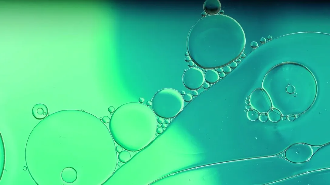 A colorful drop of oil moving on the surface of water with bubbles and spheres flowing around it 